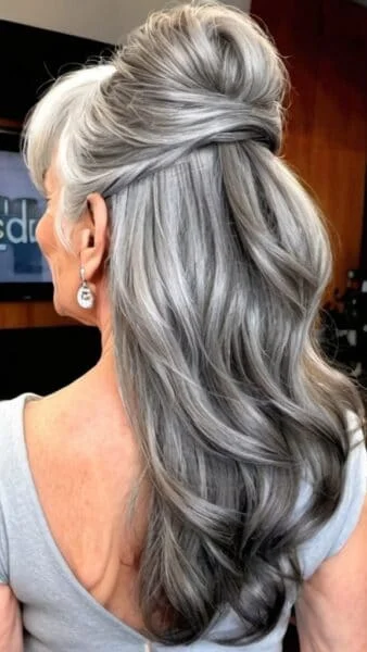 Elegant gray hairstyles for women over 60: a woman with long, wavy gray hair styled in a half-updo, wearing a light gray top.